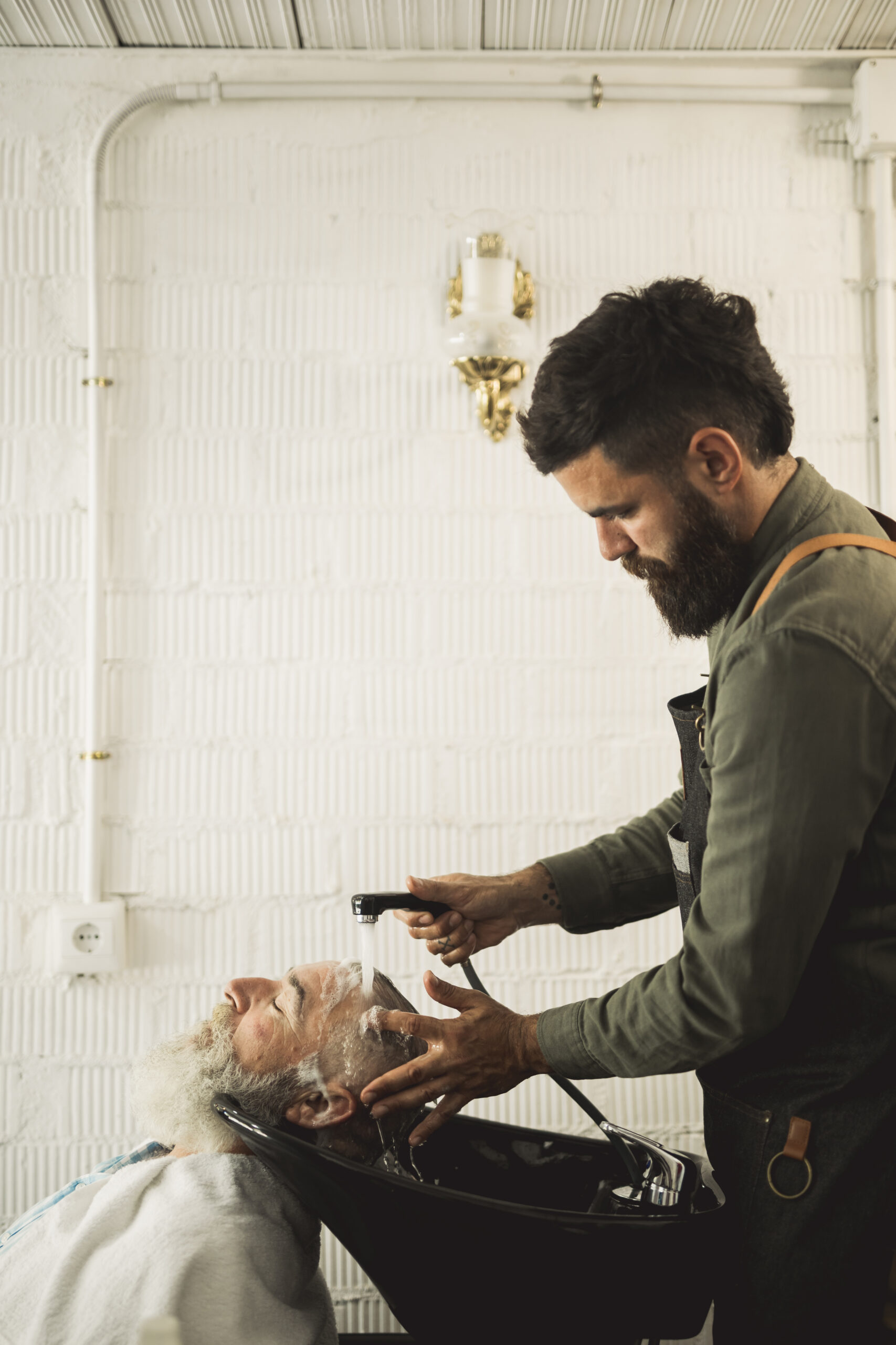 adult barber washing old man hair backwash